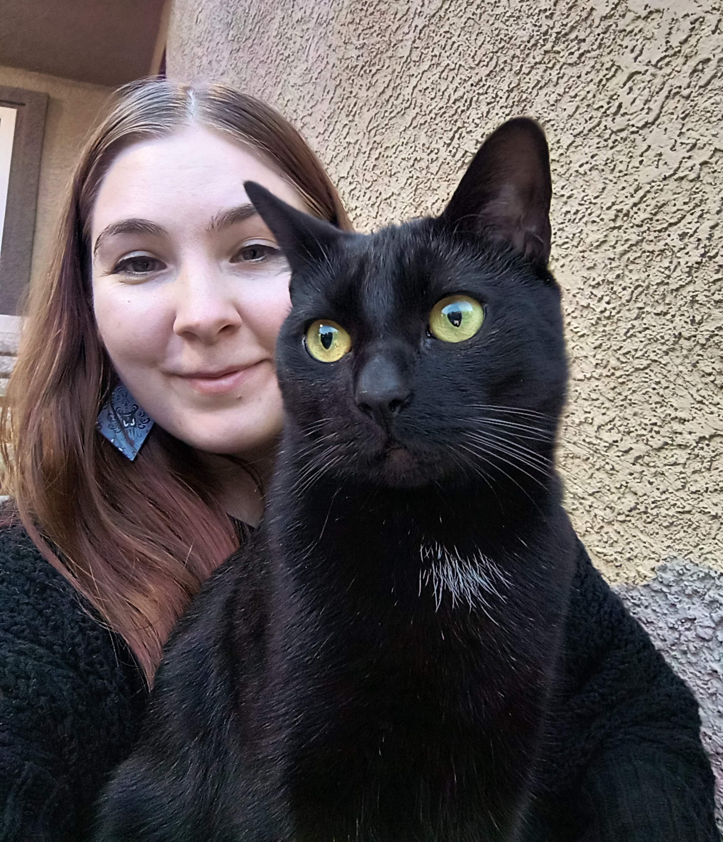 Photo of a black cat sitting on a woman's lap on an outdoor staircase.